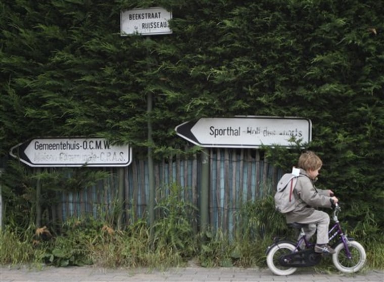A young boy rides his bike past public signs in Wezembeek-Oppem, a Flemish town near Brussels and a flashpoint of linguistic strife where francophone language signs are routinely defaced.